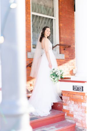 A smiling bride in a white wedding dress standing on brick steps. Holly Hotel