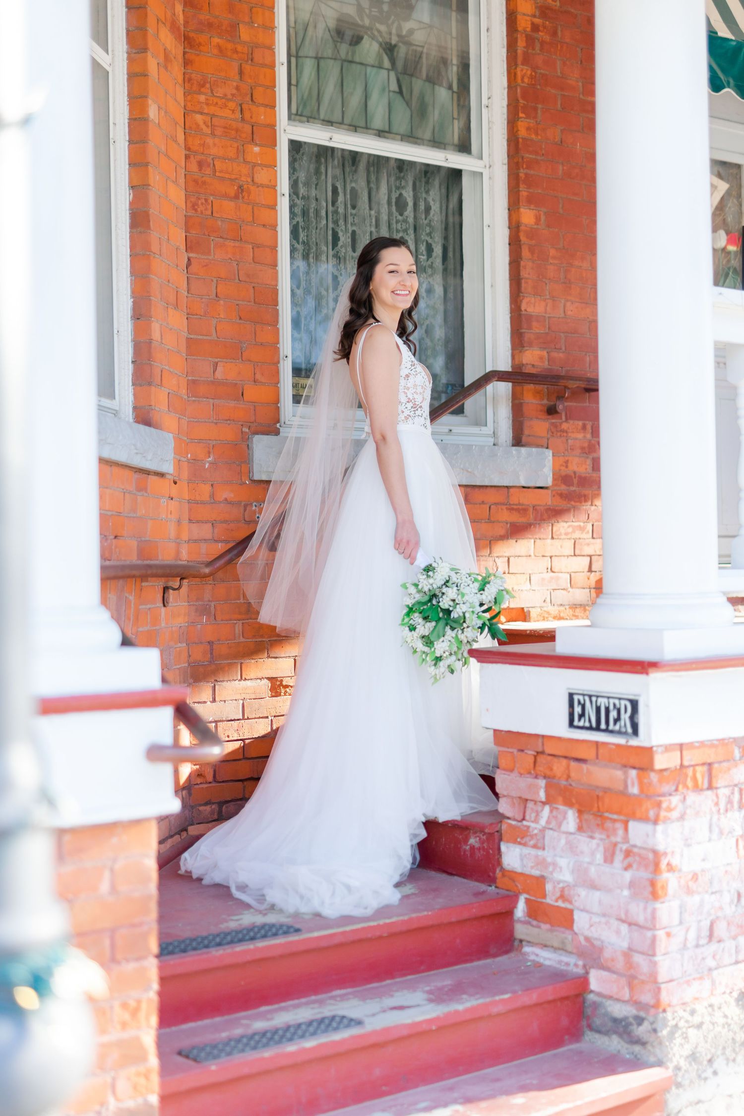 A smiling bride in a white wedding dress standing on brick steps.