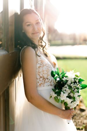 A woman in a white wedding dress stands in a garden, holding a bouquet of flowers and smiling.