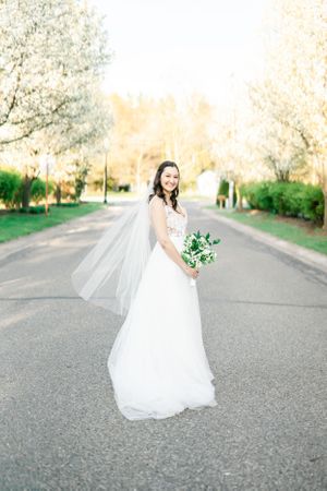 A woman in a white wedding dress walks down a path in a garden, holding a bouquet of flowers.