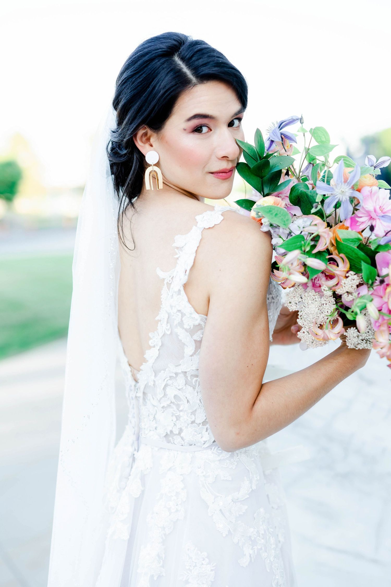 A woman in a white wedding dress holds a bouquet of flowers and looks at the camera with a smile.