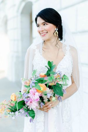 A woman in a white wedding dress holds a bouquet of flowers and smiles at the camera.