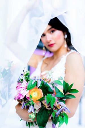 The image shows a woman wearing a white wedding dress and holding a colorful bouquet of flowers.