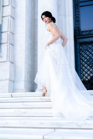 The image shows a woman wearing a white wedding dress and standing on steps.