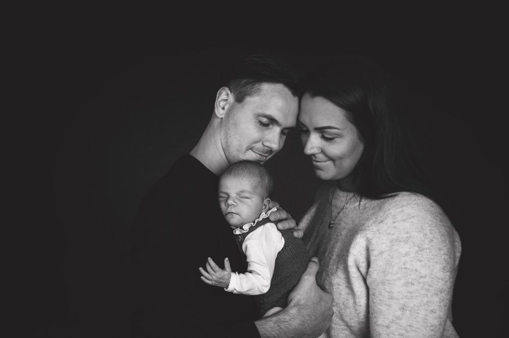 Intimate black and white family portrait with newborn baby in soft lighting.