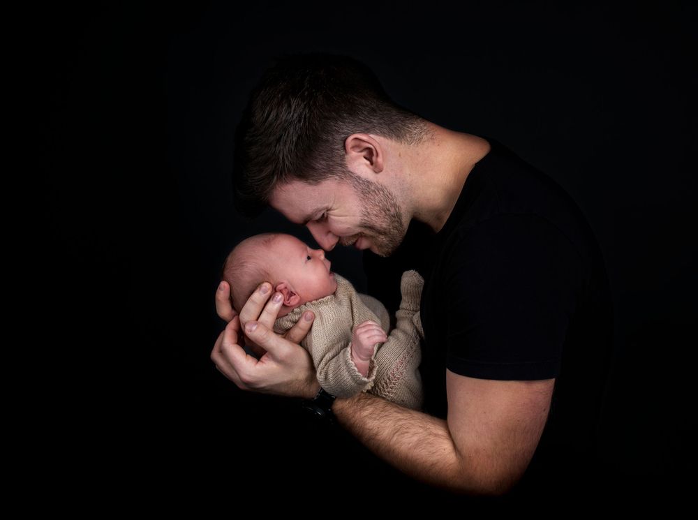 Intimate black and white portrait of parent nuzzling newborn baby against dark background.