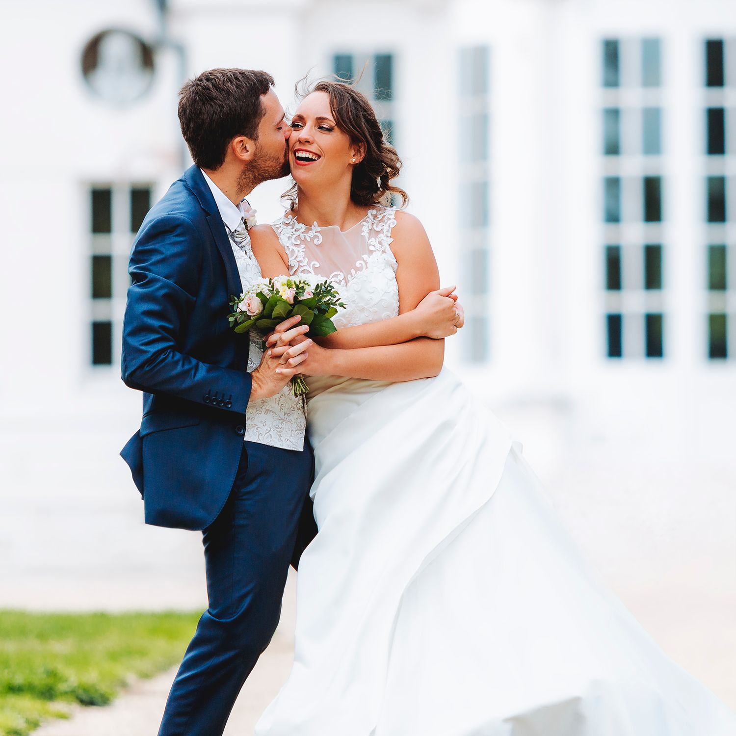 A tender wedding moment captured outside a white building.