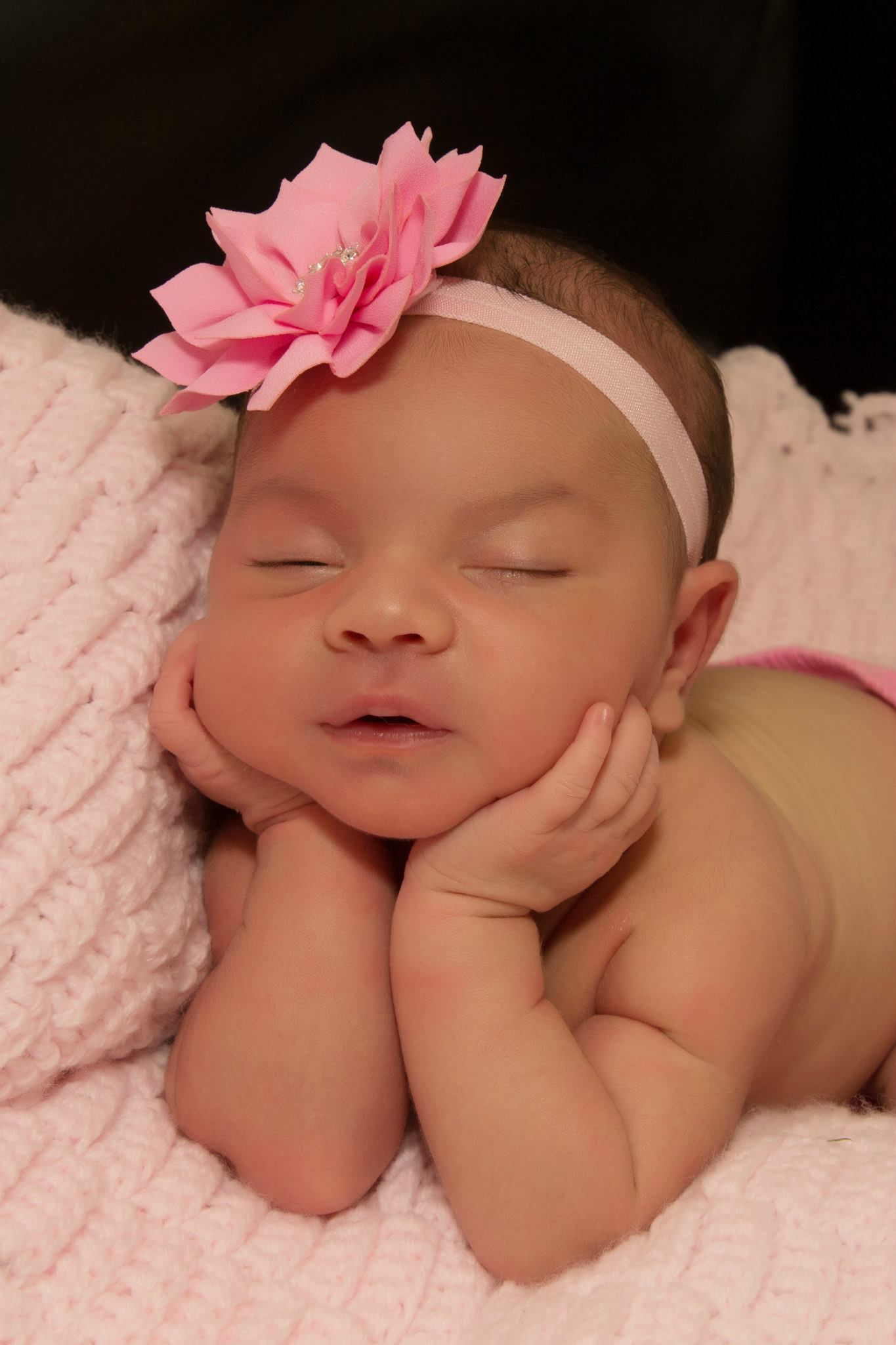 Sleeping baby on white blanket with pink headband accessory.