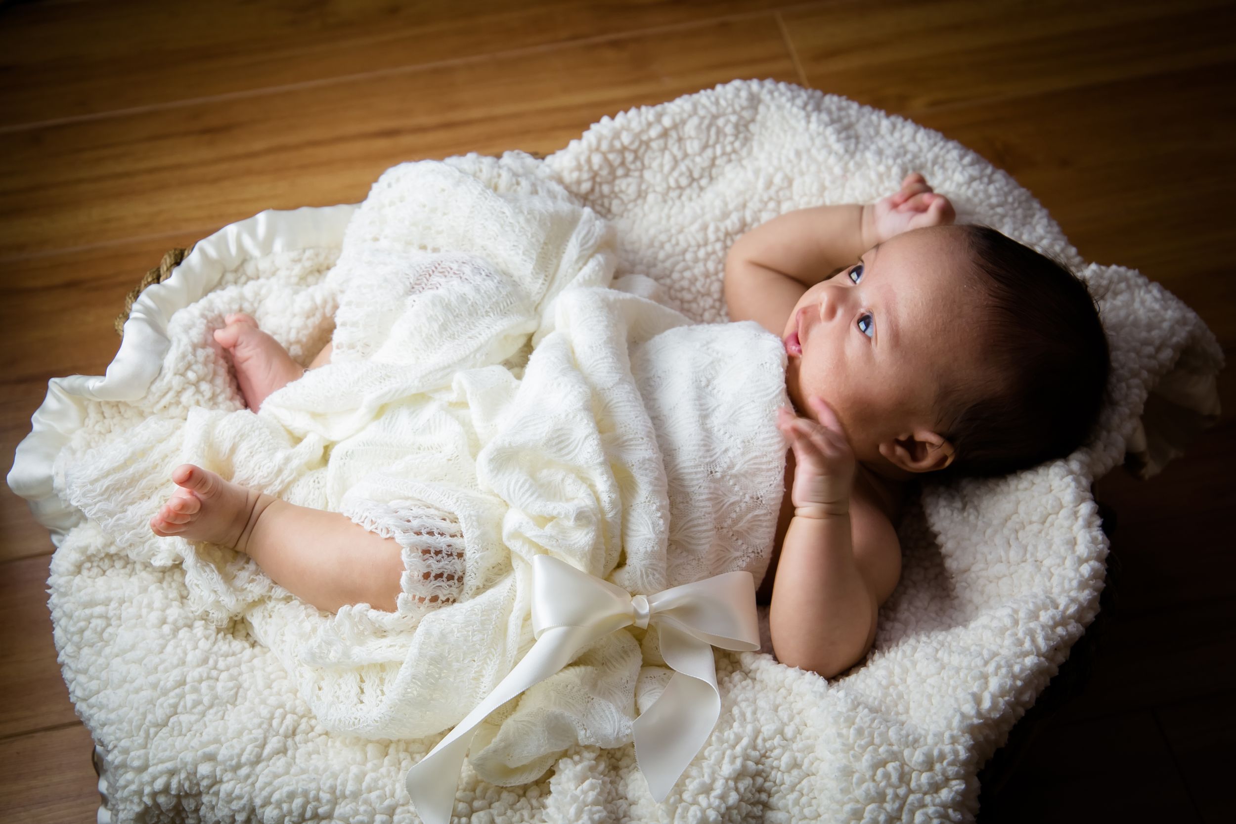 Sleeping newborn wrapped in delicate white lace on wooden floor.