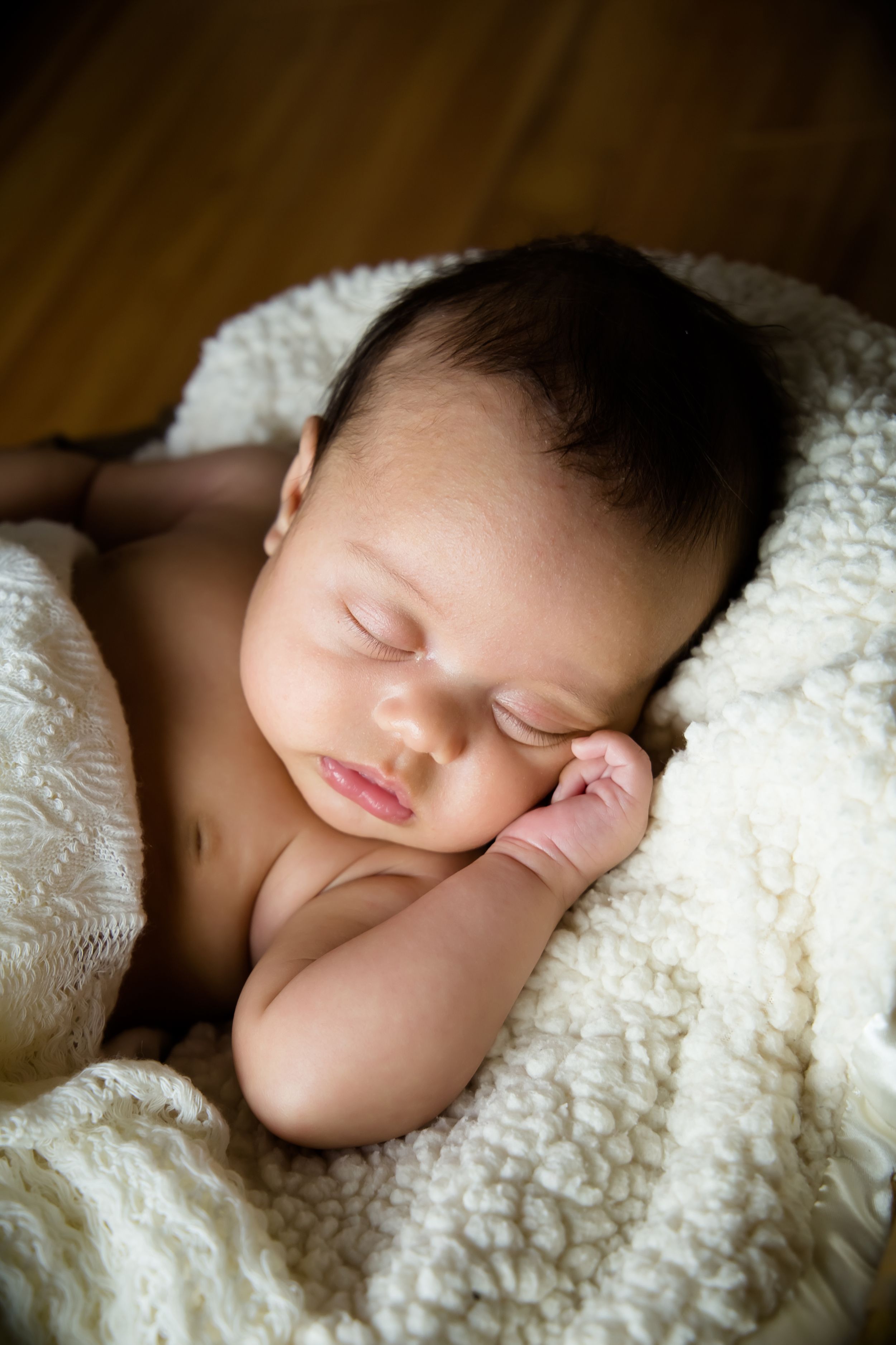 Peaceful sleeping baby nestled in cream colored textured blanket.