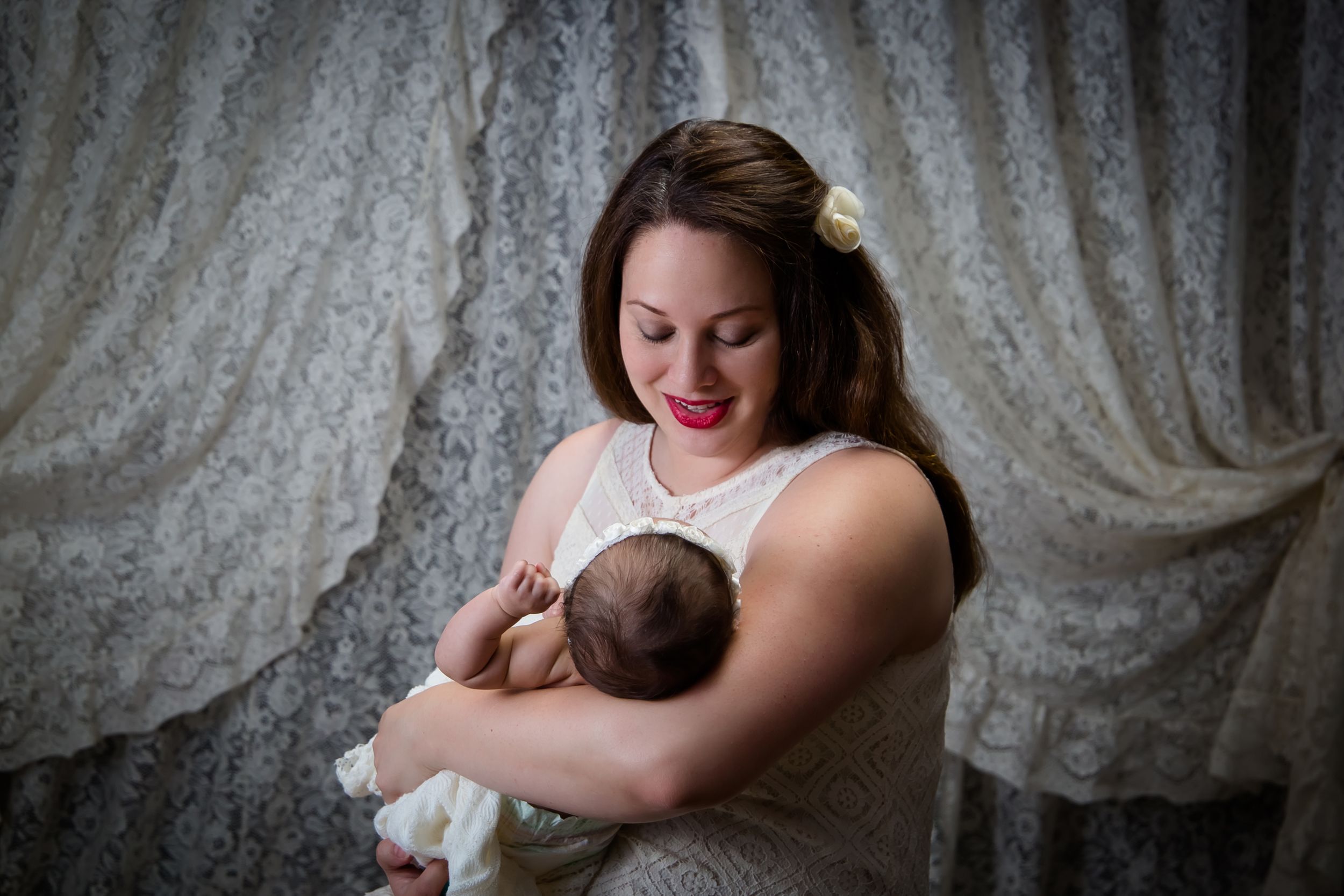 A tender moment captured during breastfeeding against a backdrop of lace curtains.