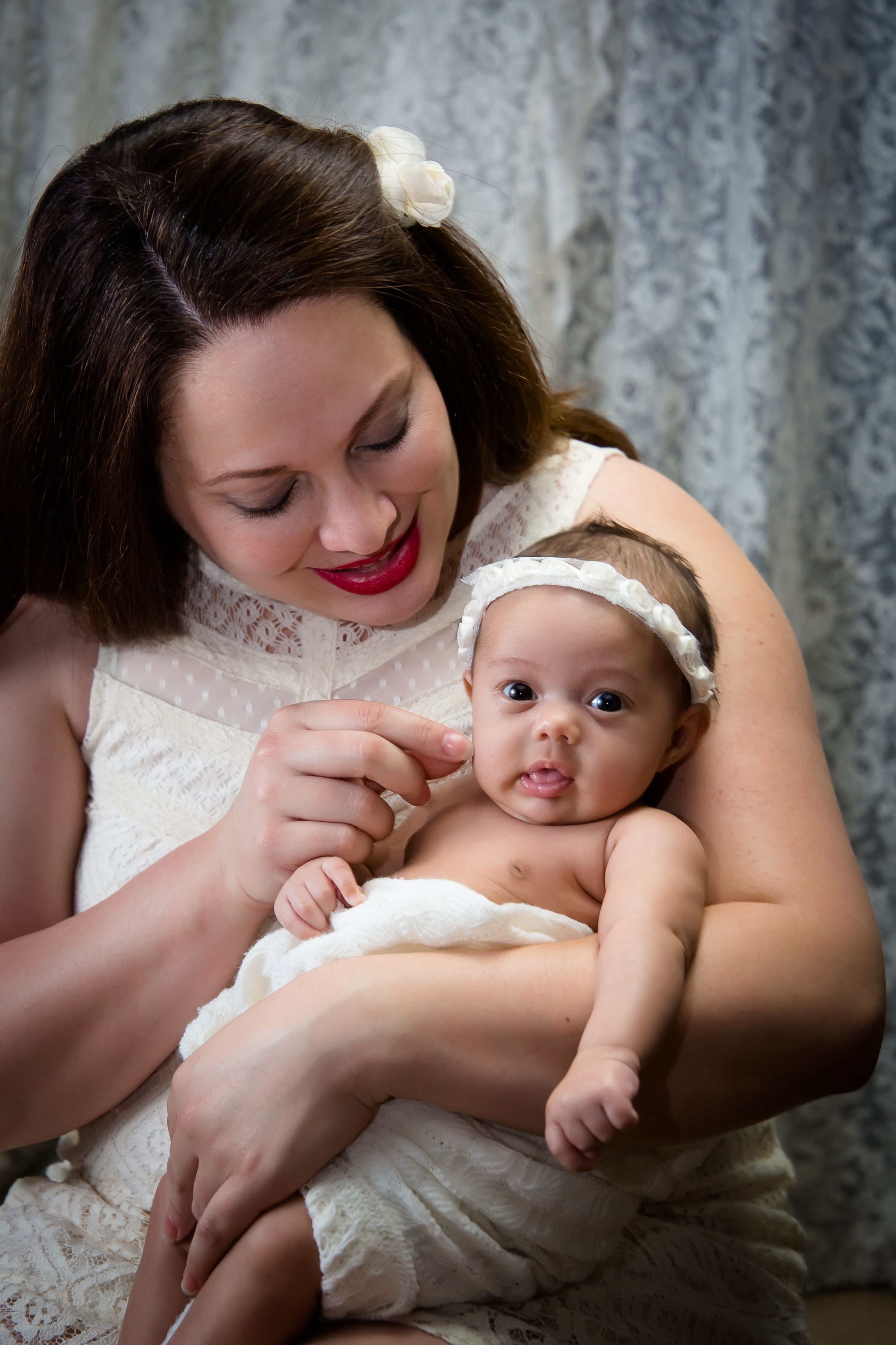 Tender moment between mother and baby against lace curtain background.