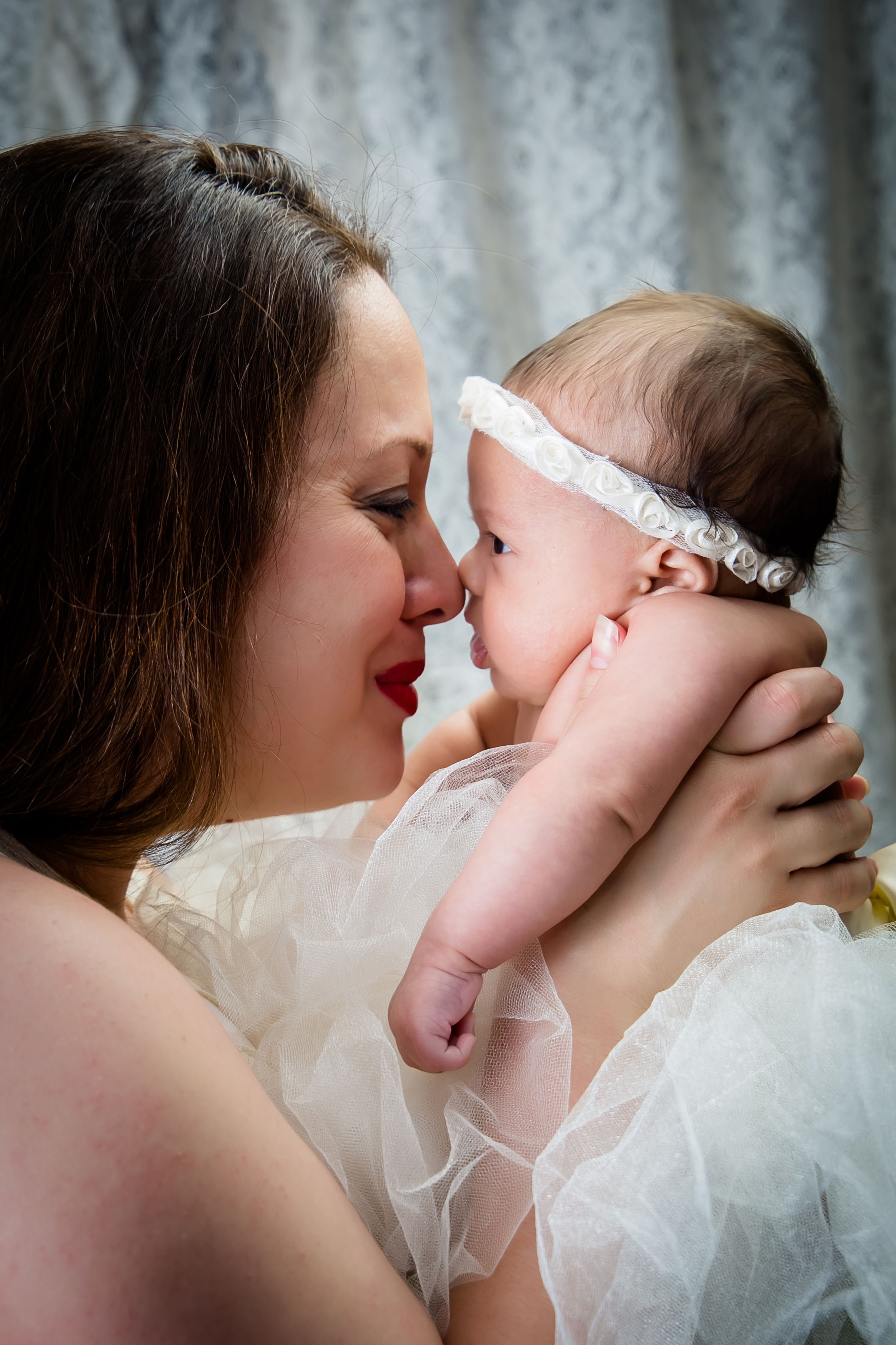 Sweet bonding moment captured in soft natural light with white lace details.