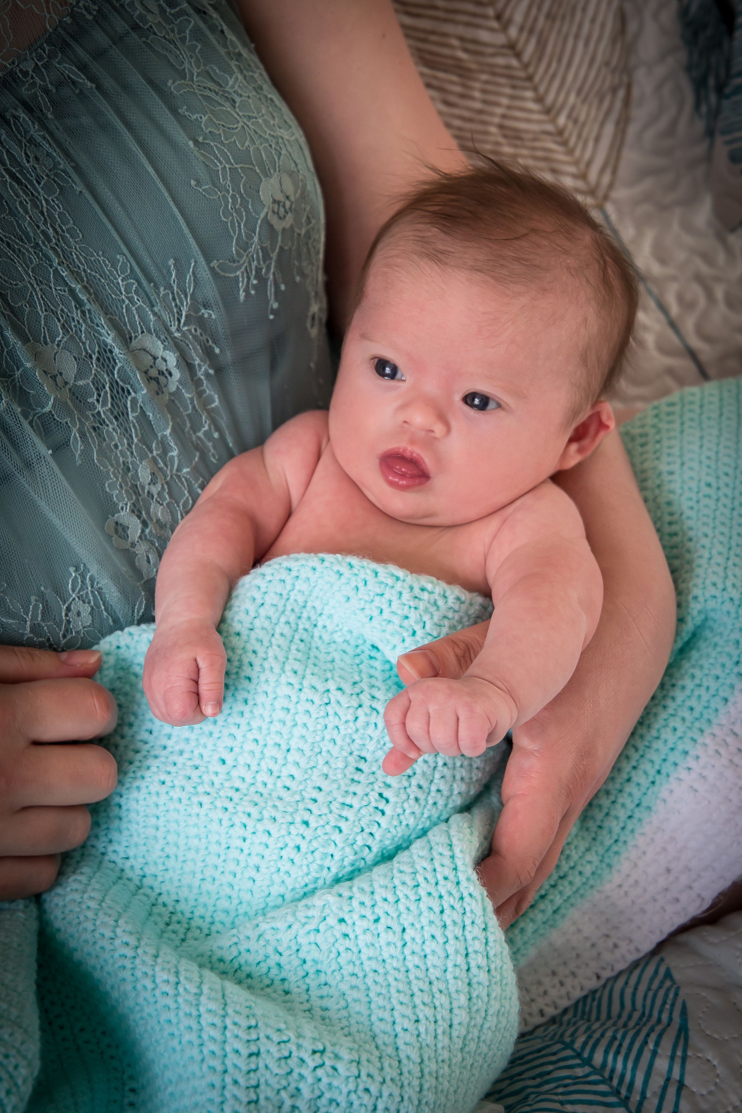 A baby lies on a mint green knitted blanket looking up with curiosity.