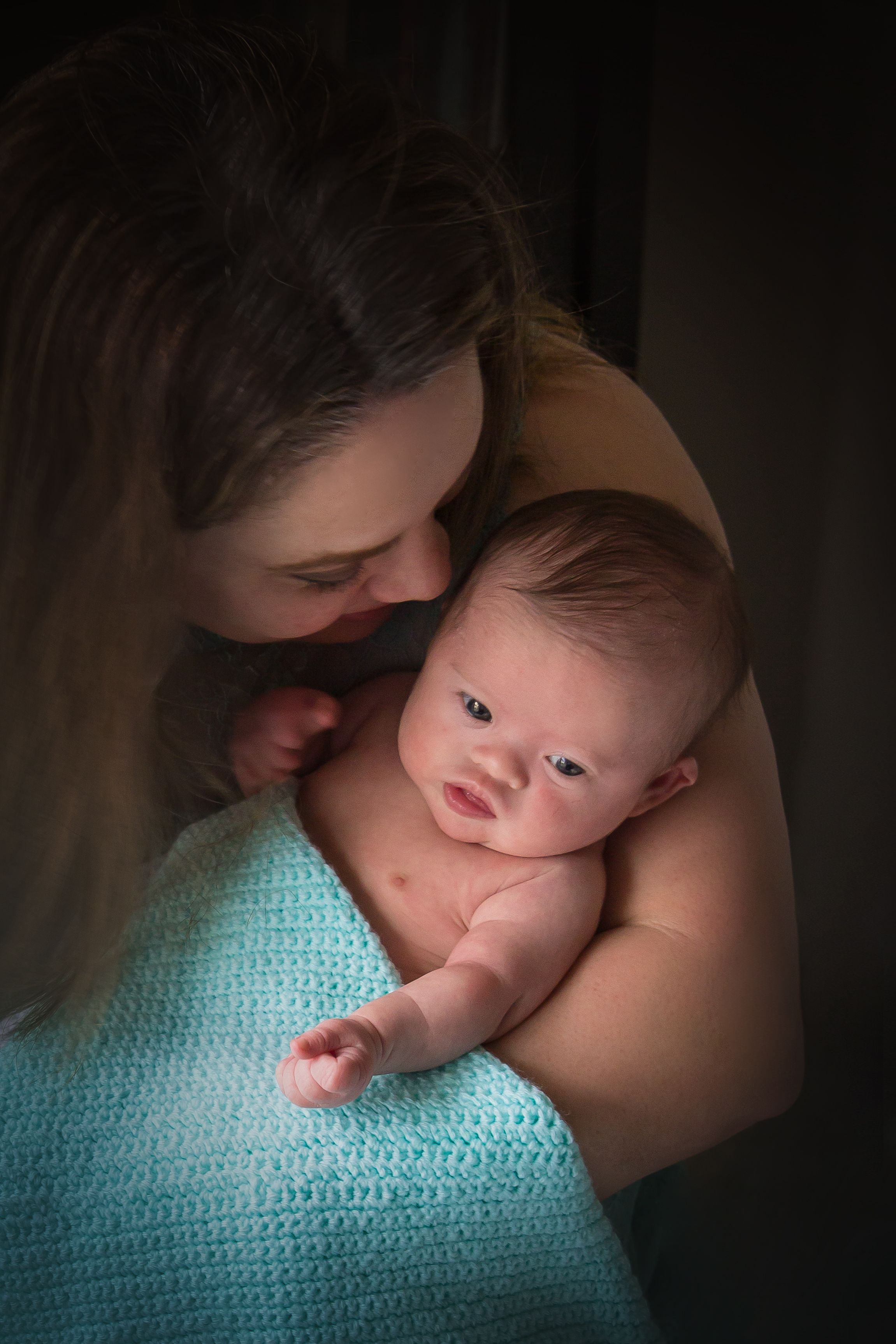 A dramatic portrait of a baby resting on turquoise fabric in moody lighting.