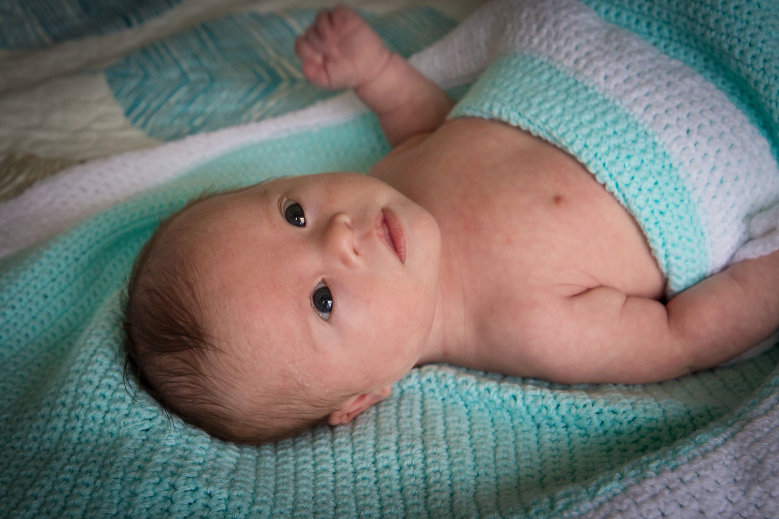 Baby lying on turquoise knitted blanket in series of peaceful poses.