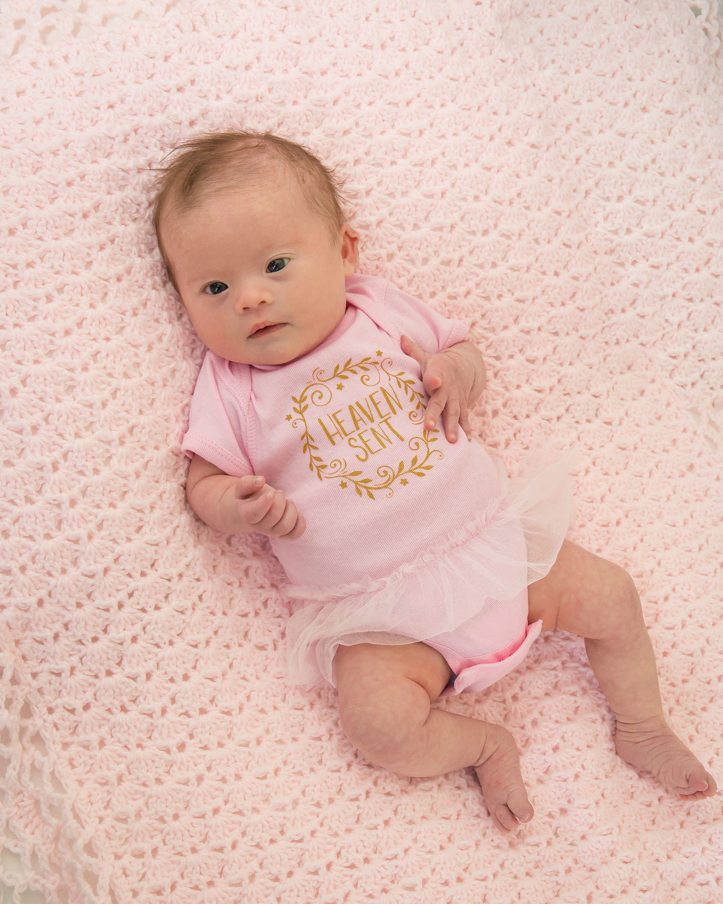 Infant wearing pink outfit lying on soft textured pink blanket.