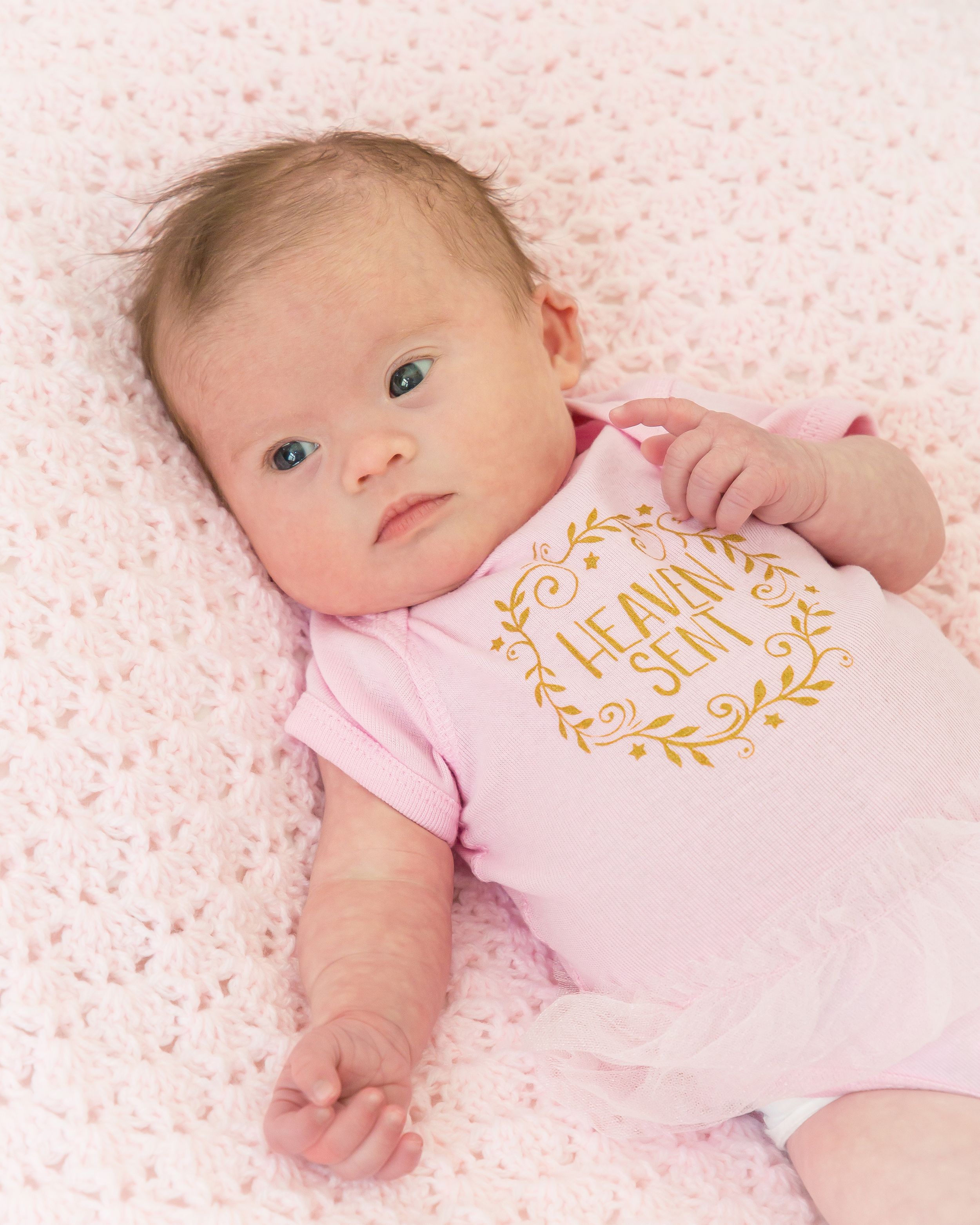 A baby in a pink outfit rests on a soft pink patterned blanket.