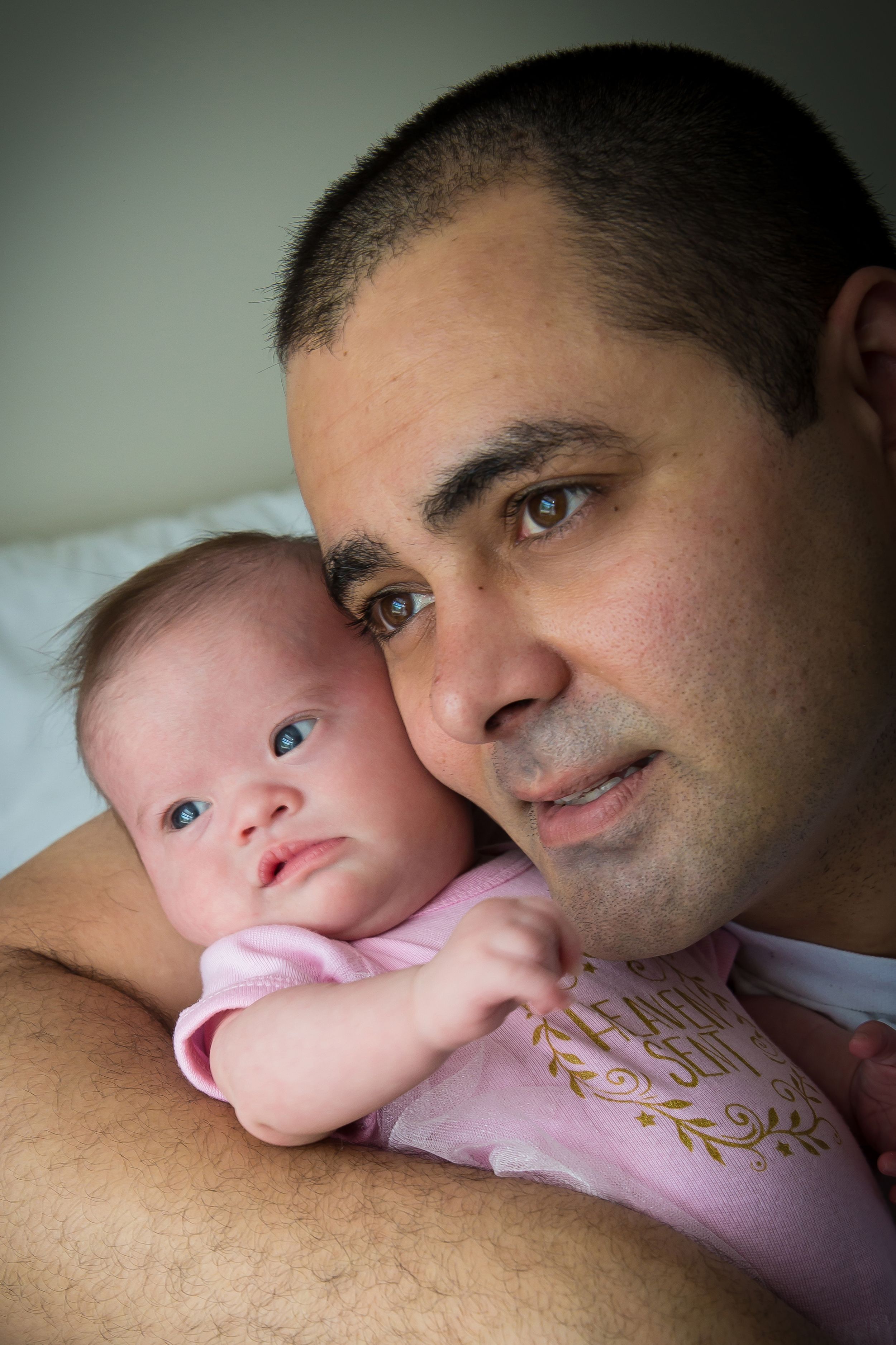 Tender moment between parent and baby on pink blanket in soft lighting.