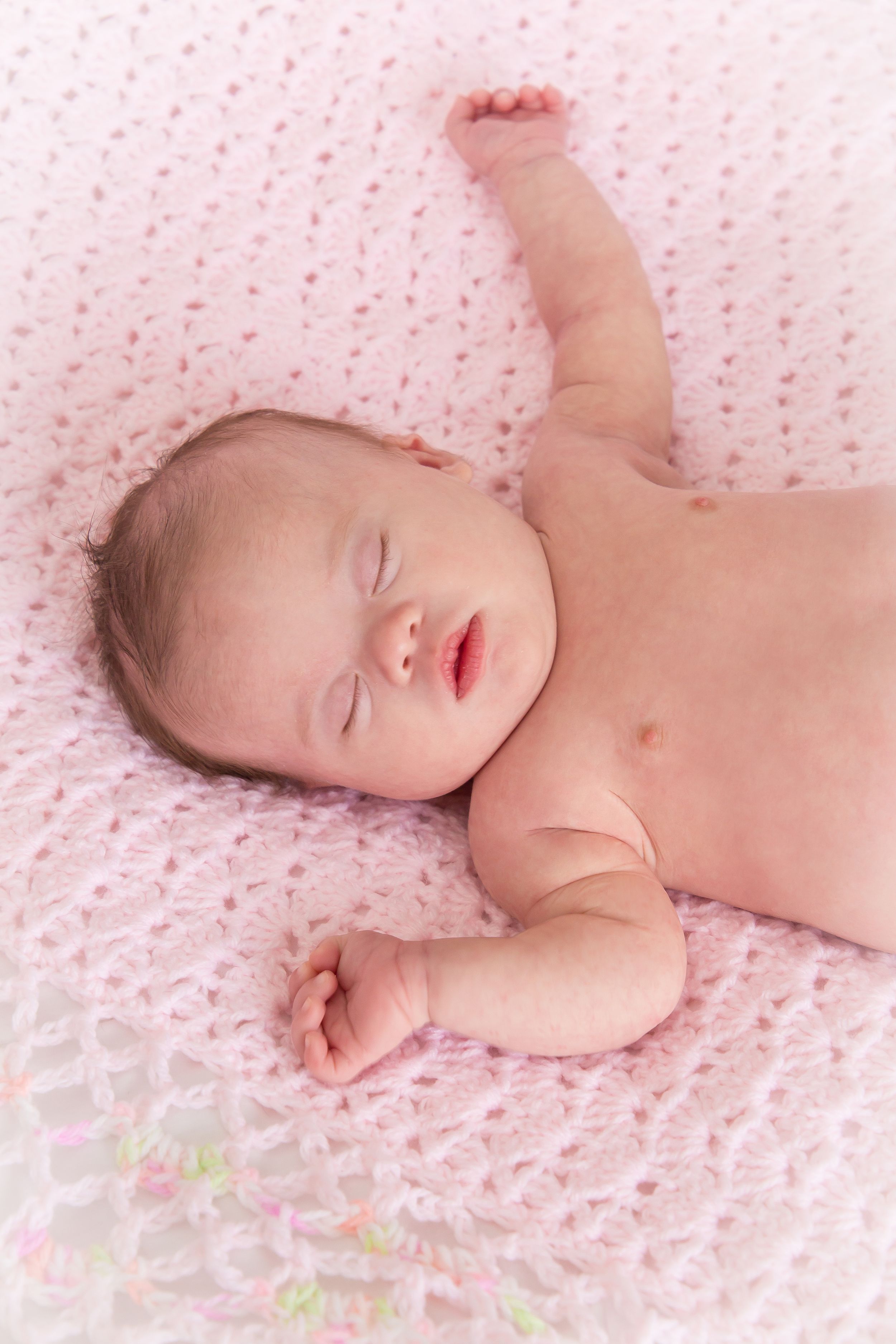 A sleeping baby lies peacefully on a pink dotted blanket in a series of gentle poses.