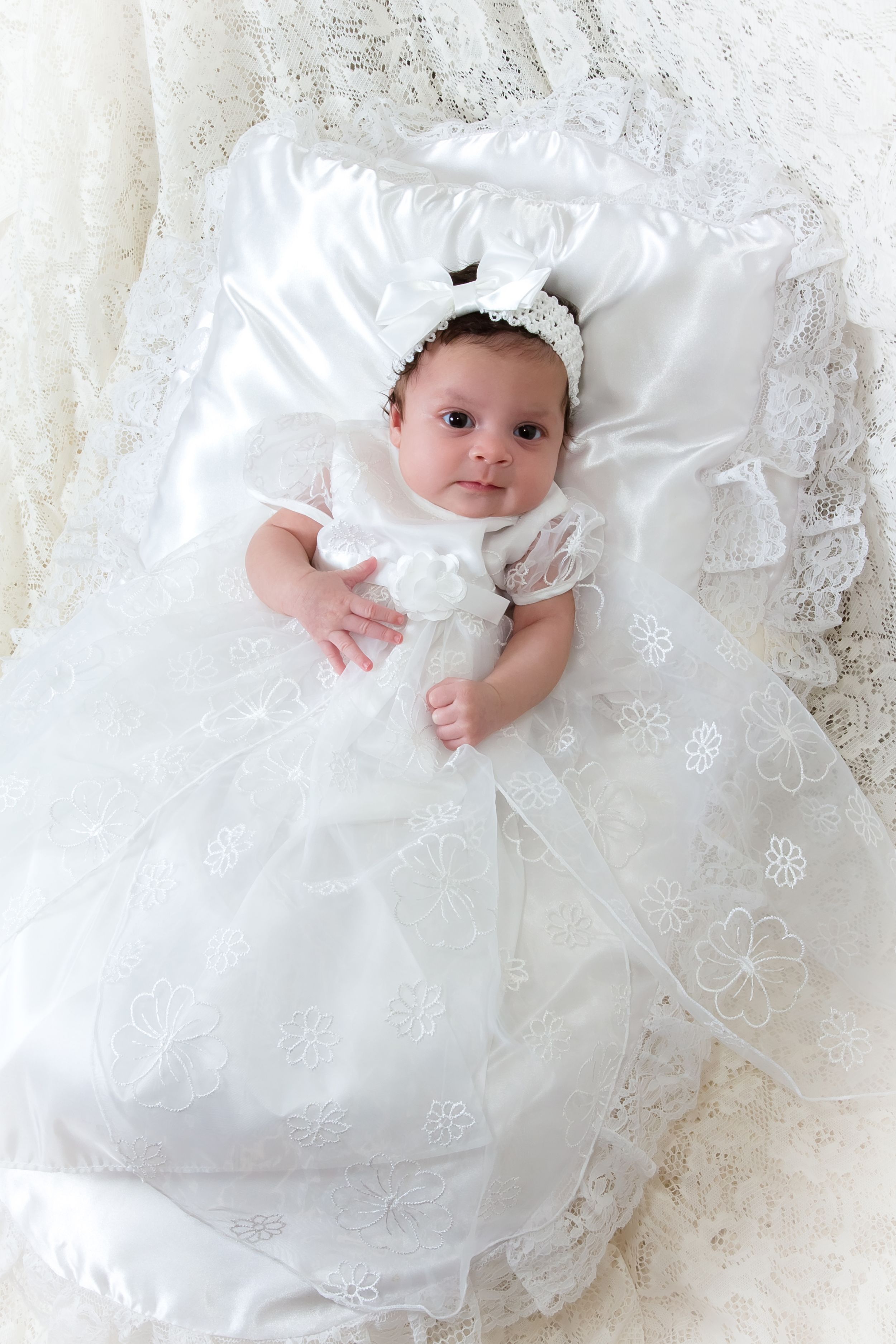 Baby wearing traditional white christening outfit on lace background.