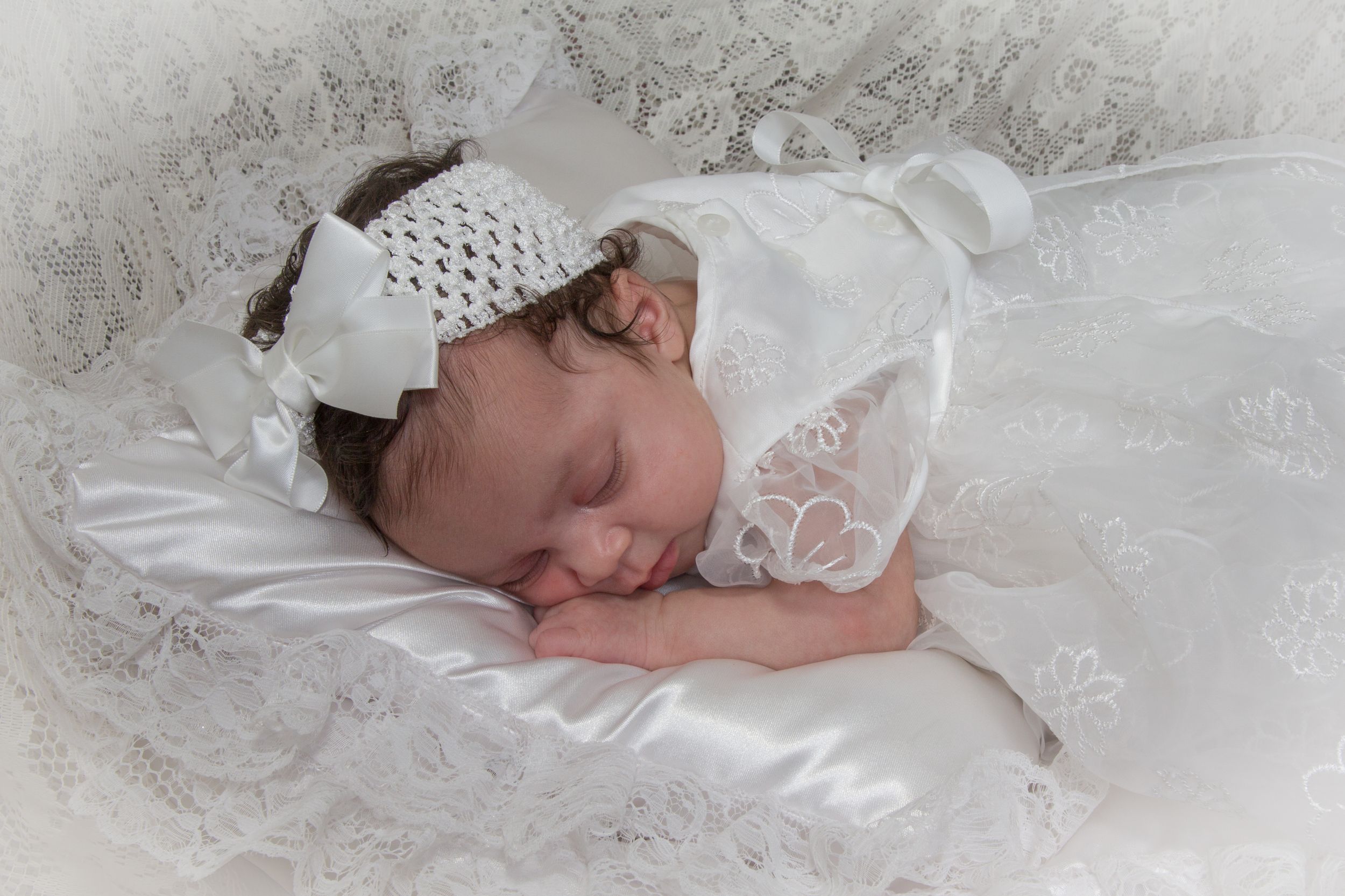 Infant in white baptismal gown resting on delicate lace fabric.