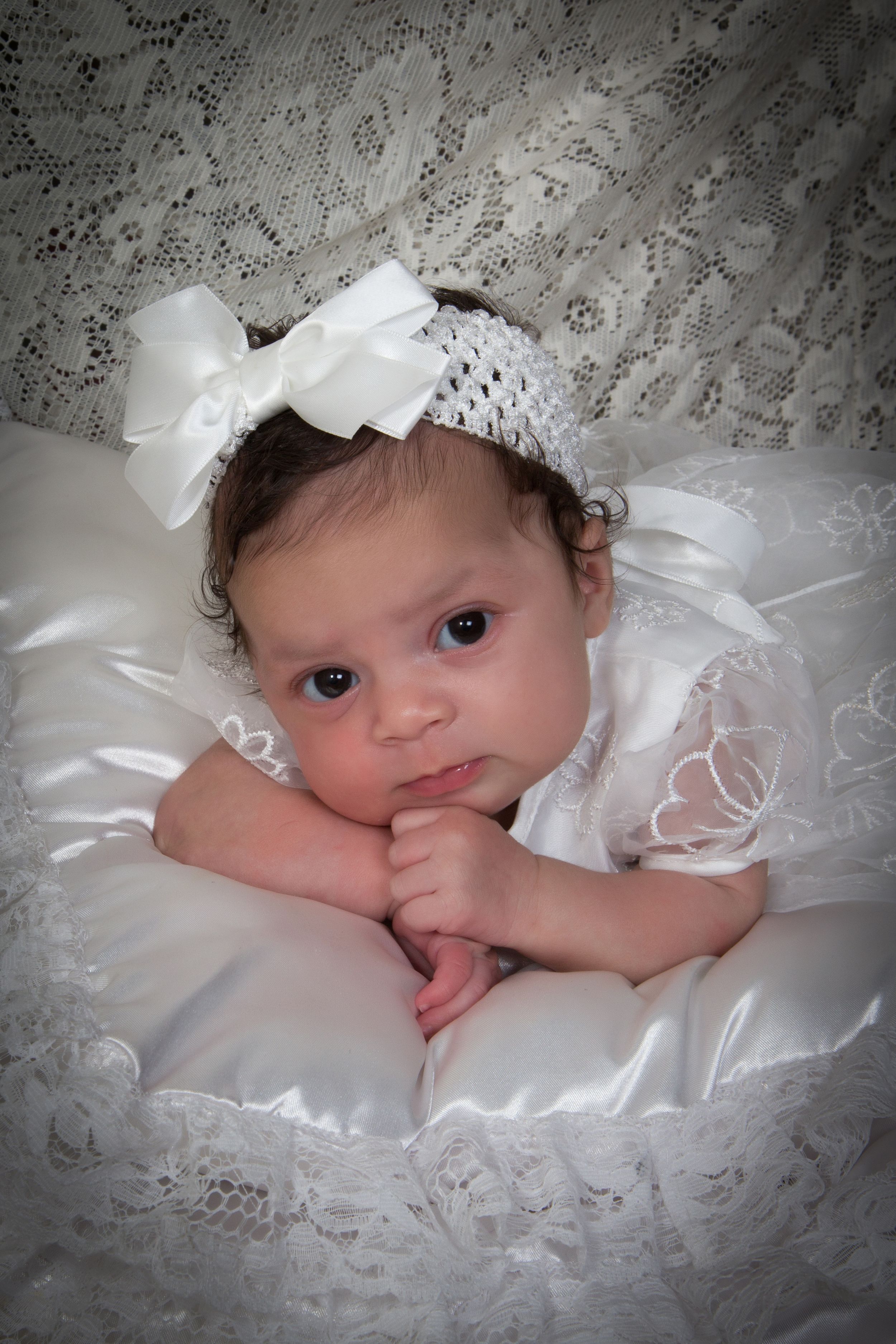 Baby in delicate white lace bonnet resting on satin fabric.