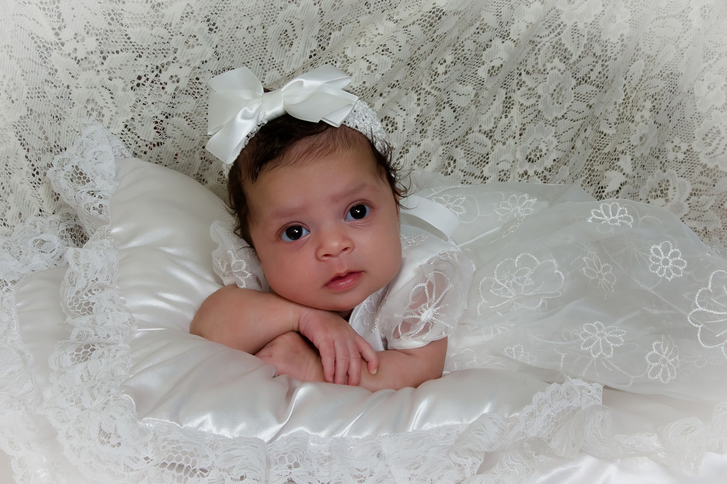 Infant in white baptismal attire nestled in delicate lace.