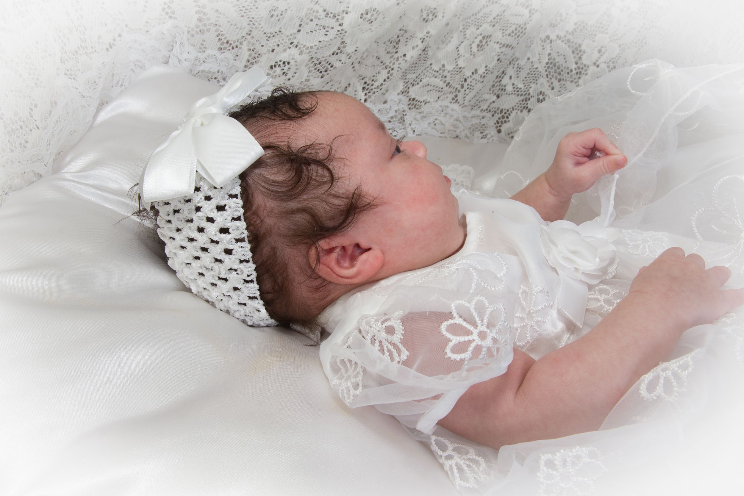 Newborn wearing white lace bonnet against soft white background.