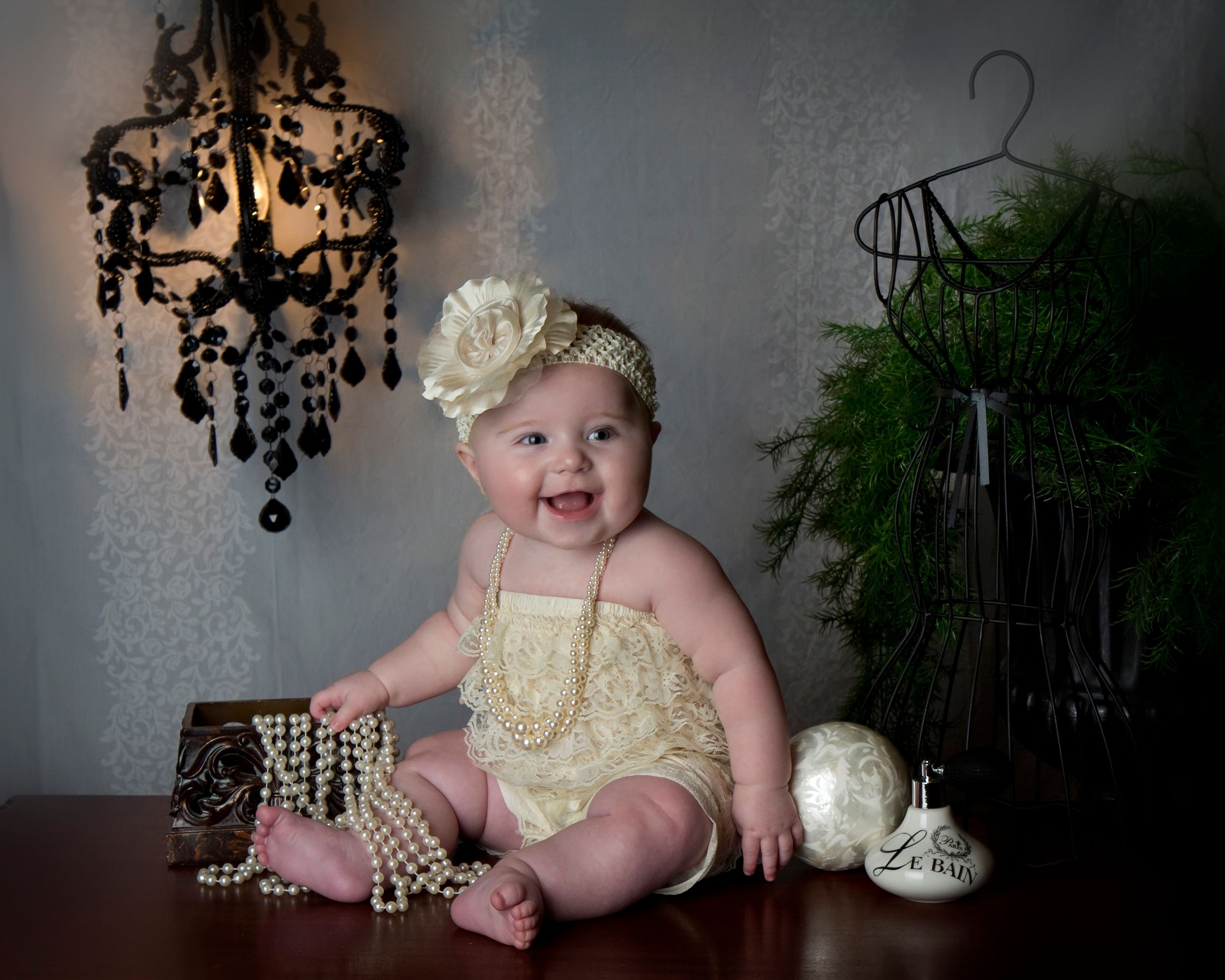 Baby in cream outfit smiling near chandelier and decorative accessories.
