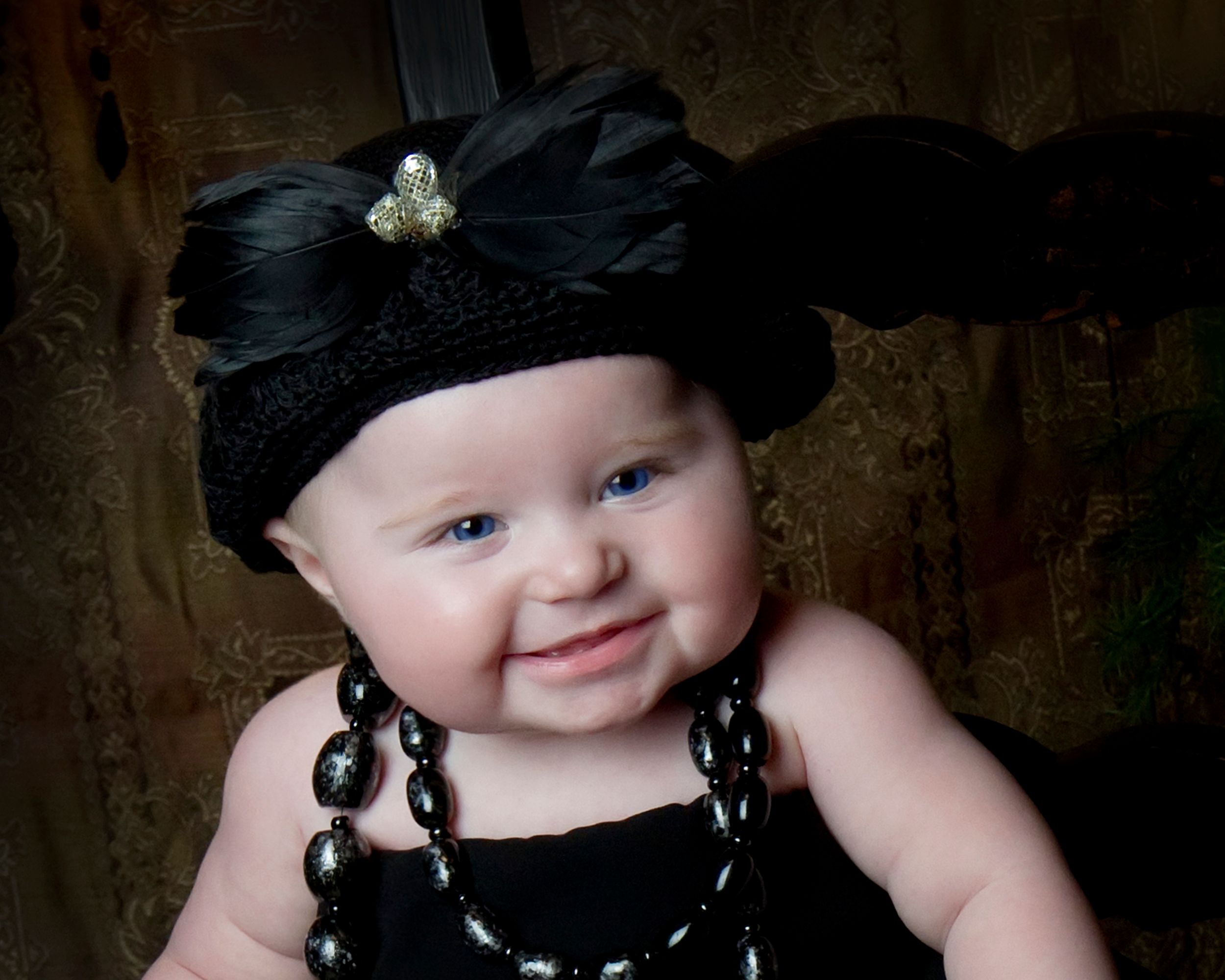Baby wearing black headband and beaded necklace with sweet smile.