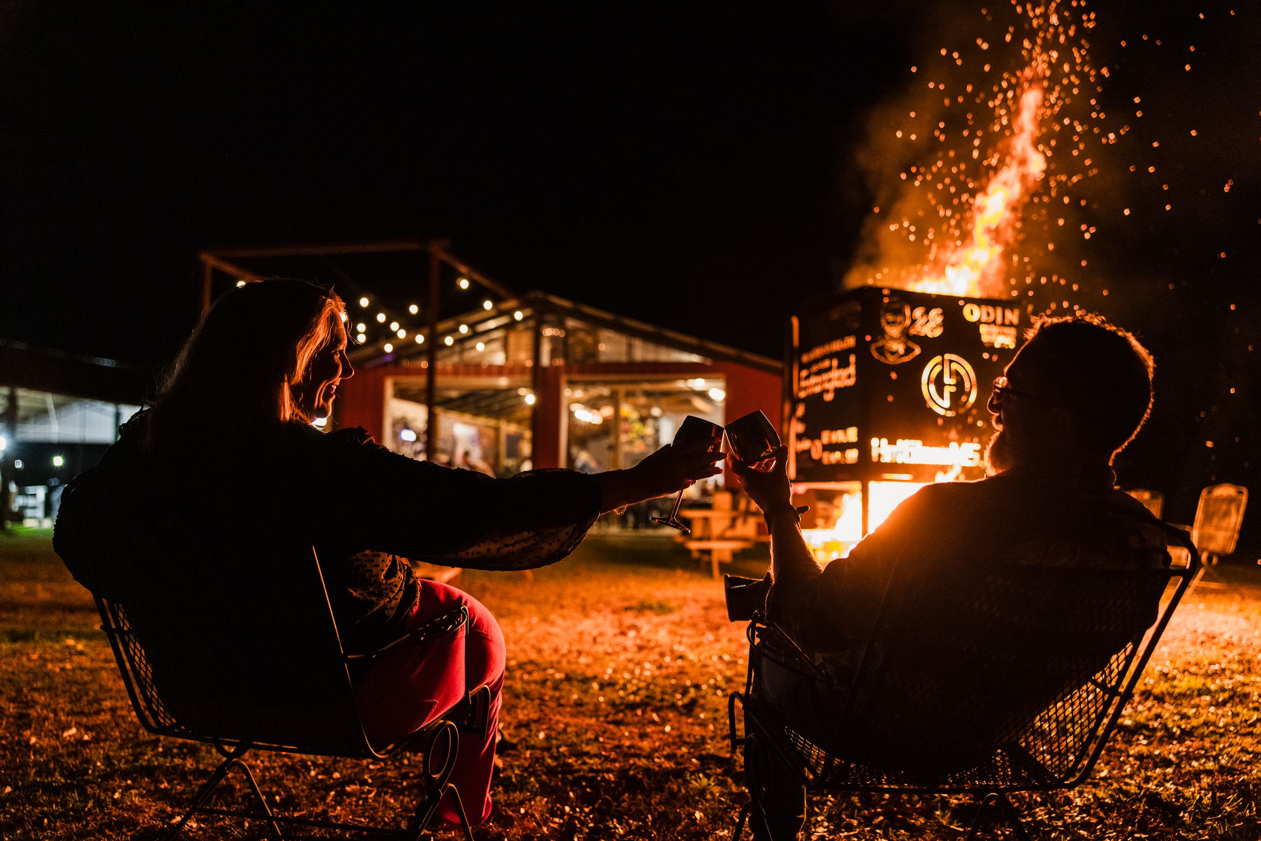 Nighttime campfire scene with glowing embers and sparks against a dark background.