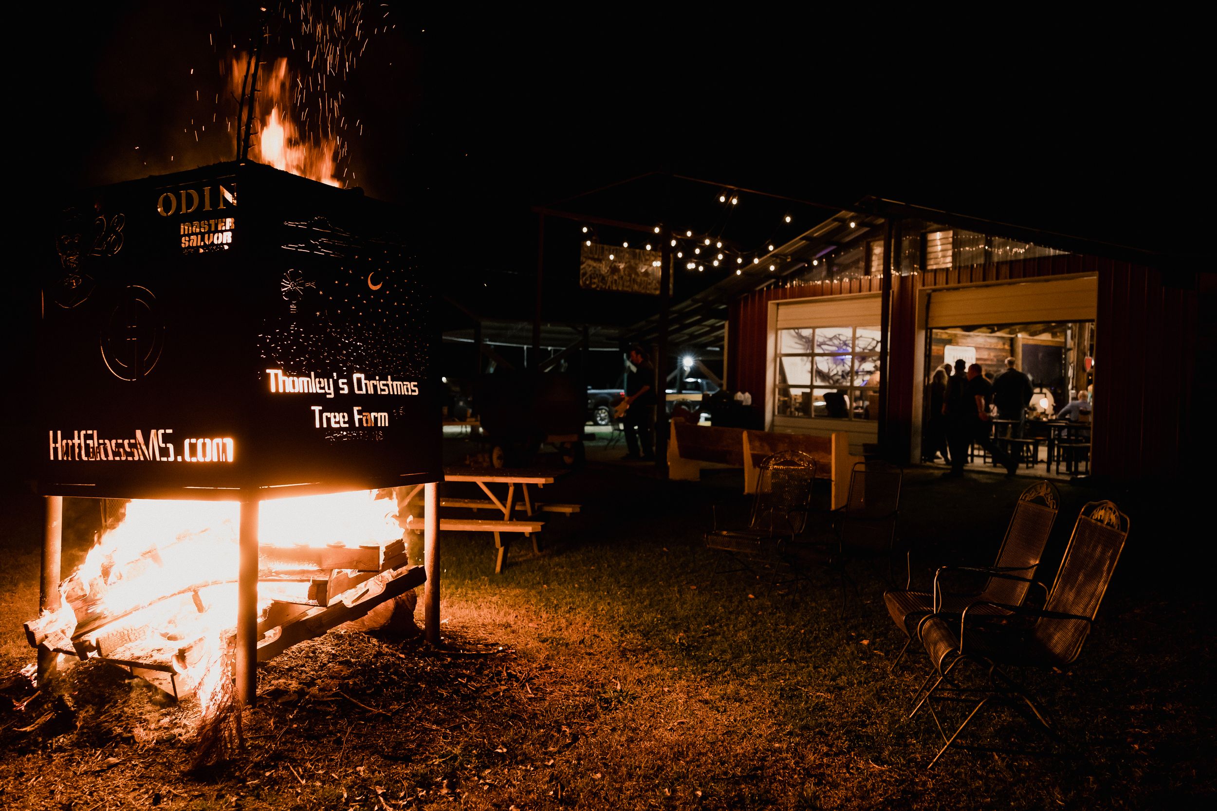 Wide view of an outdoor nighttime scene with warm lighting and distant fires.