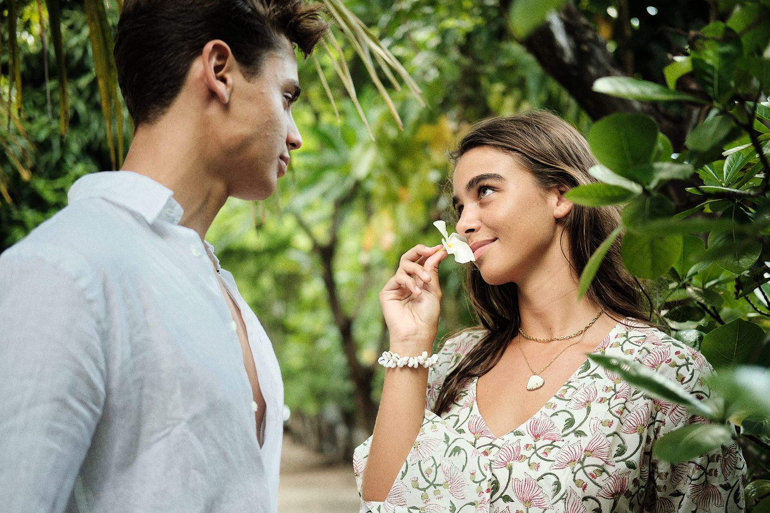Jeune couple se regardant dans les yeux. Elle hume une fleur de Tiare Tahiti. Shooting photo couple éditorial pour le Hine Magazine