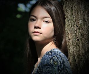 Artistic portrait of someone leaning against a tree trunk in a blue patterned dress.