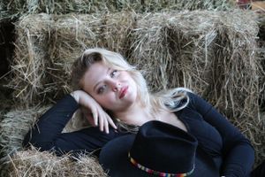Someone reclining on hay bales wearing a black top and hat in a relaxed countryside photo shoot.