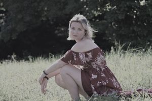 Vintage-style portrait of someone in a floral dress sitting in summer grass.