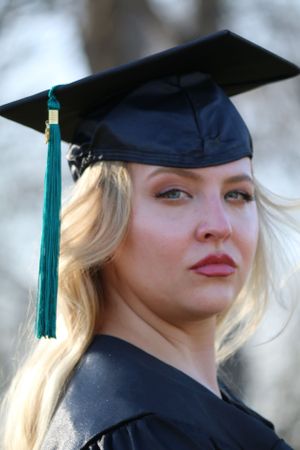 Graduate wearing a traditional black cap with green tassel and graduation gown in an outdoor setting.
