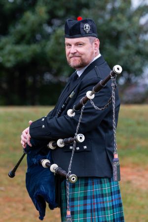 Bagpiper in traditional Scottish attire with green and blue tartan kilt performing outdoors.