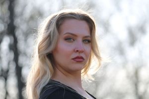 A person with blonde wavy hair in a black top poses outdoors during golden hour.