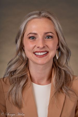 Professional headshot in a tan blazer and white top against a neutral backdrop.
