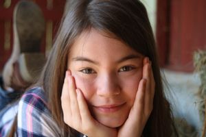 Indoor portrait of someone in plaid shirt resting face in hands with gentle expression.
