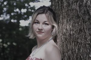 Artistic outdoor portrait taken against a tree trunk in natural lighting.