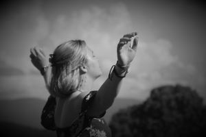 Black and white artistic photo of raised arms against a cloudy sky.