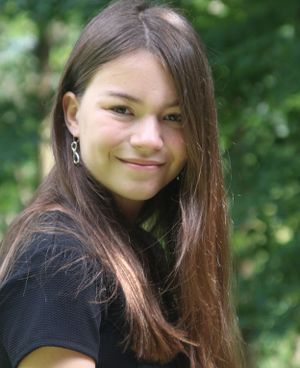 Portrait of someone with long brown hair smiling warmly against a blurred green background.