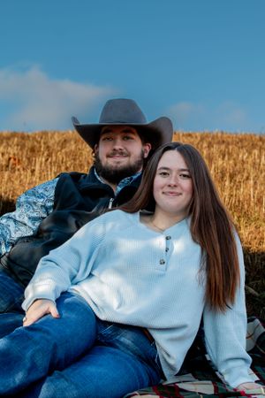 A couple enjoys an autumn afternoon sitting together in front of a golden wheat field under a blue sky.