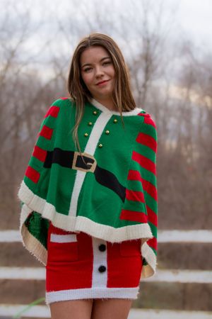 Festive holiday sweater dress in green and red with white trim worn outdoors against a winter forest backdrop.