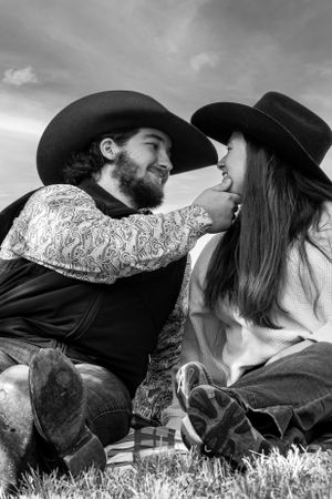 A romantic black and white western scene shows a couple in cowboy hats sharing an intimate moment while resting in the grass.