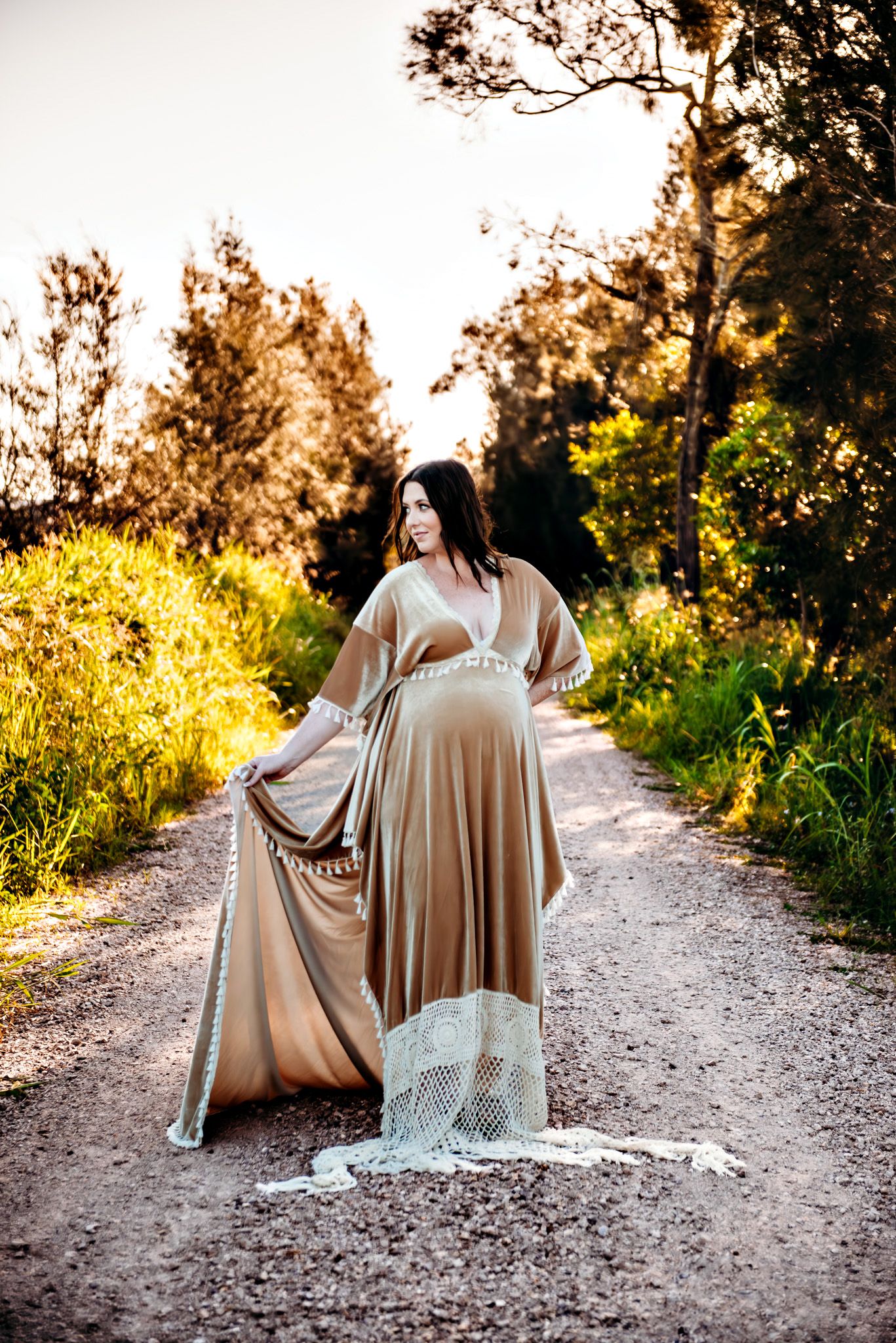 A flowing beige dress cascades down a dirt path during a golden hour photoshoot.