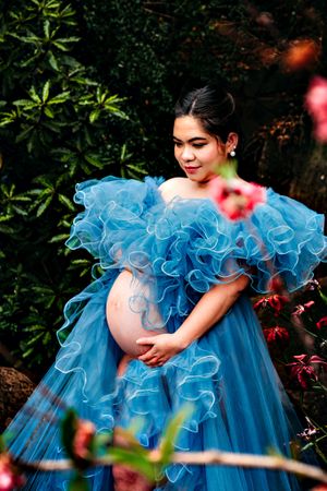 Ruffled blue princess gown photographed in lush garden setting with pink floral accents.